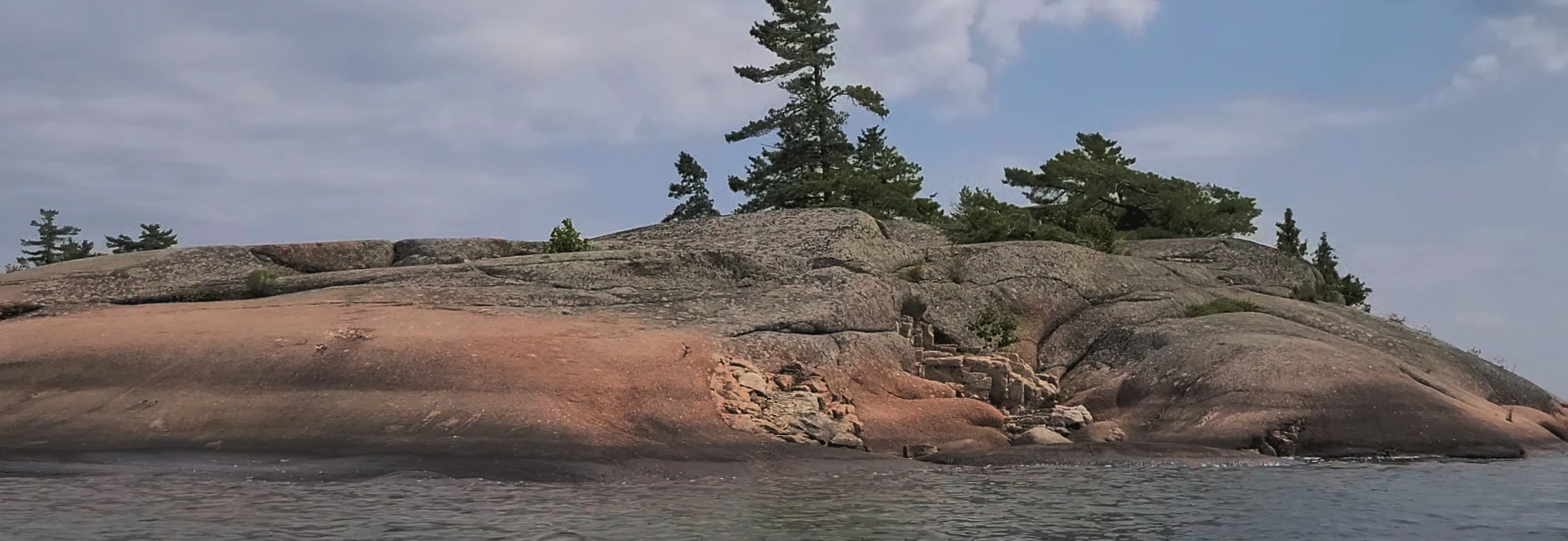 Western Shoreline of the Benjamind islands with red granite rock, white quartzite,
                trees and clear water